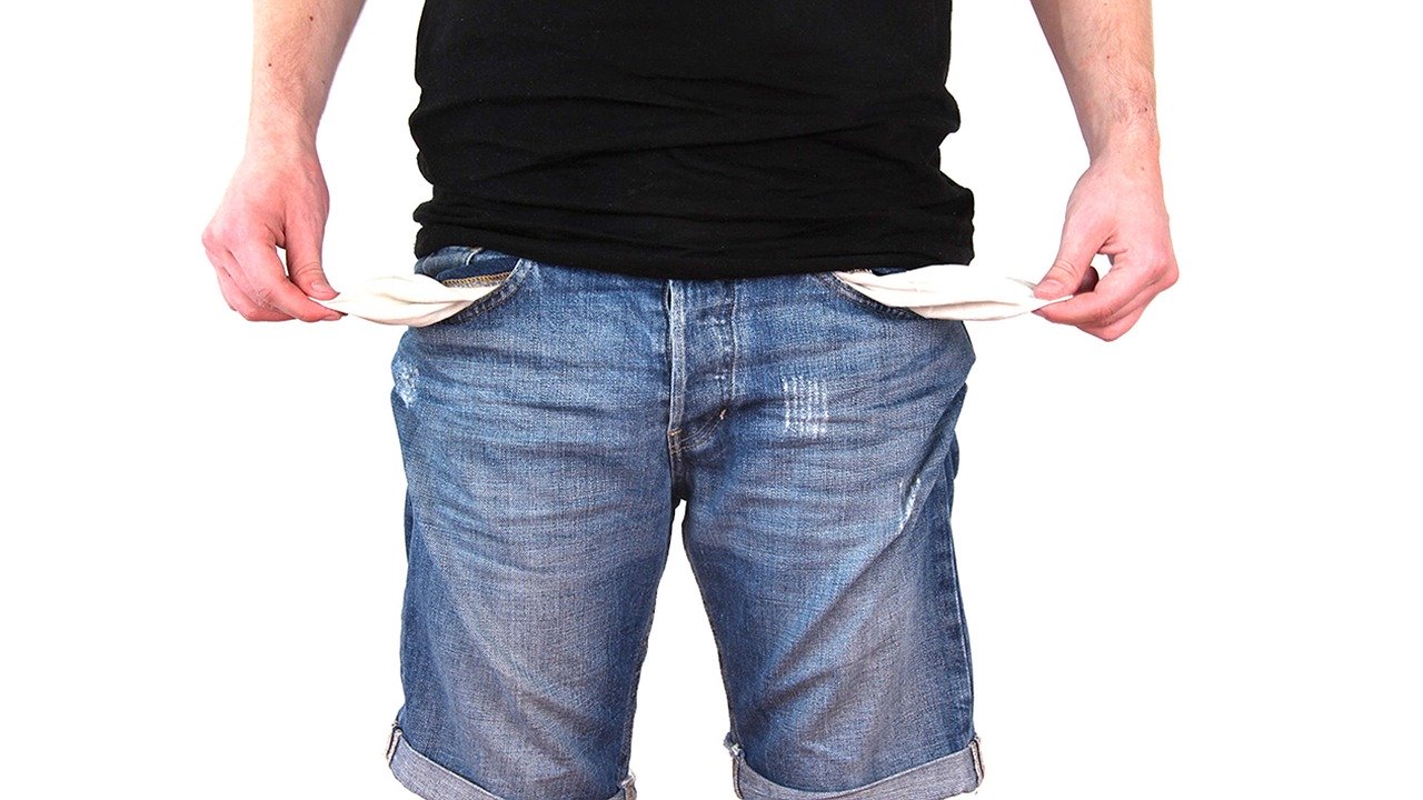 Person mit kurzer blauer Jean und schwarzen T-Shirt zieht die Innentaschen seiner Hose raus um die Leere zu symbolisieren