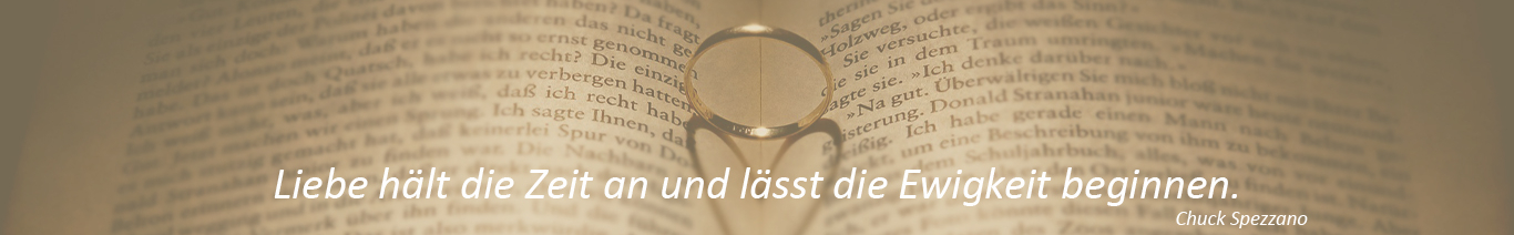 Aufgeschlagenes Buch, in der Mitte einen Ring der einen herzförmigen Schatten wirft, Spruch: Liebe hält die Zeit an und lässt die Ewigkeit beginnen.