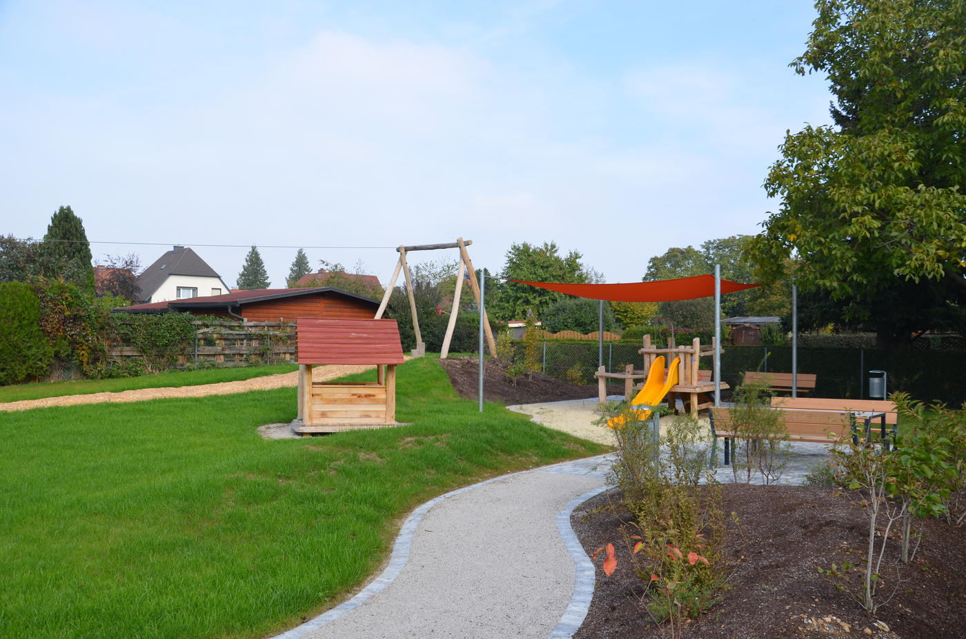 Spielplatz mit gelber Rutsche und einem gepflasterten Weg