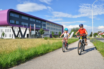Zwei Kinder mit Fahrrad und Helm auf einem Radweg in Leonding