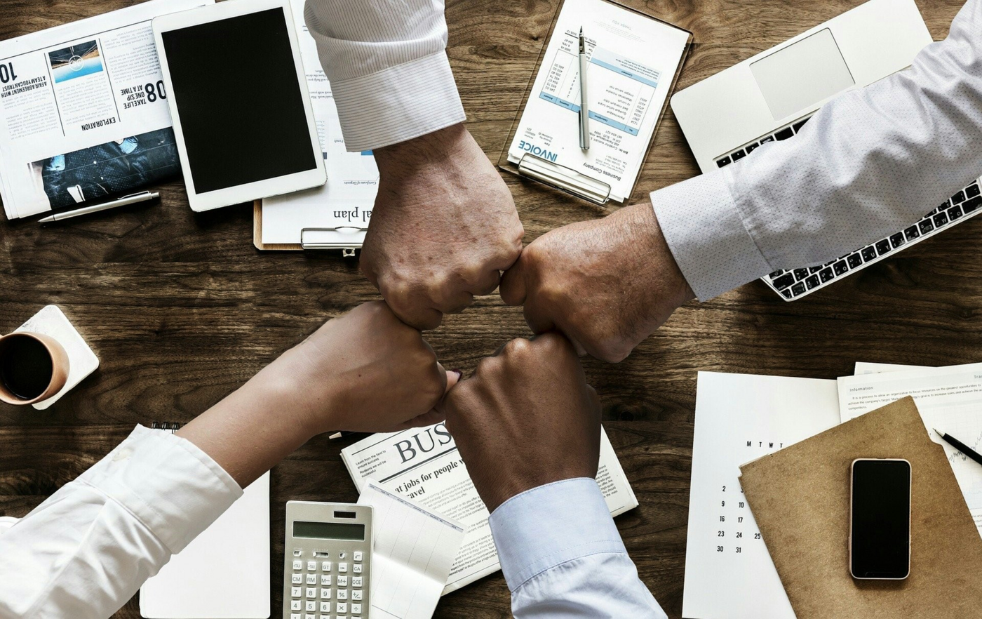 4 Fäuste treffen in der Mitte zusammen, Untergrund Holz mit diversen Büromaterial