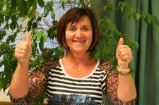 Magda Bäck steht vor einem Strauch und zeigt mit beiden Daumen nach oben